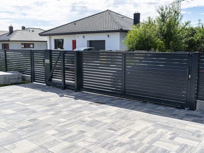 A modern panel fence in anthracite color, a visible sliding gate to the garage and a wicket with a letterbox.