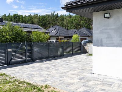 A modern panel fence in anthracite color, a visible sliding gate to the garage and a wicket with a letterbox.